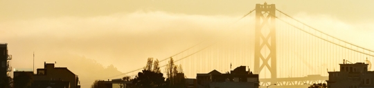 Yellow skies with silhouetted houses and the golden gate bridge shape fading in the background